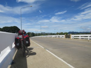 packed touring bike leaning on a brige, empty street and blue sky