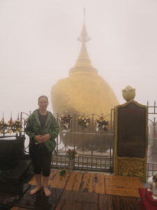 Eine Person steht barfuß. Hinter ihr ist Nebel, durch den der Goldene Felsen hervorscheint