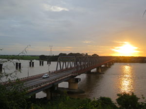 Functioning bridge as well as left-overs of a blown-up own, across a river, at sunset